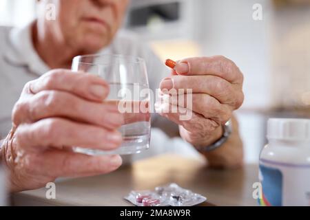Beware this troubled world, control your intake. Closeup shot of an elderly man taking medication while siting at the kitchen table at home. Stock Photo