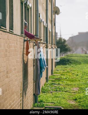 Old woman tends laundry hanging in the Portuguese sunshine in Espinho, Portugal. January 2023 Stock Photo