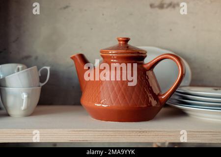 brown clay teapot on a white shelf with cups and plates Stock Photo