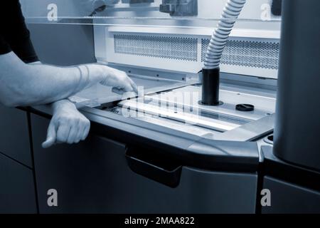 A male worker stands near the powder part of a powder 3D printer and points his finger of the hand at it. industrial production equipment. New modern 3D printing additive progressive technology MJF Stock Photo