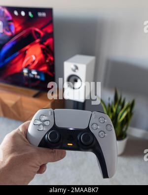 LONDON - JANUARY 06, 2023: Man playing holding PS5 PlayStation 5 games console controller by TV in modern living room Stock Photo