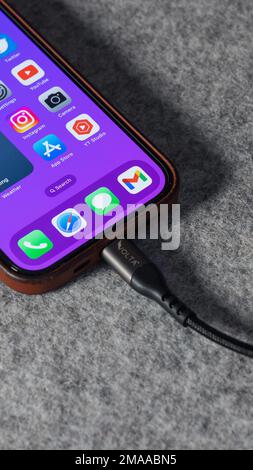 LONDON - JANUARY 10, 2023: Apple iPhone 14 Pro charging cable with home screen and app icons Stock Photo