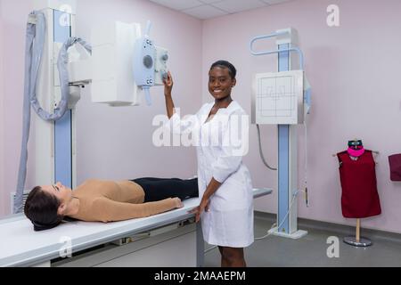 A young African-American radiologist doctor taking an X-ray of a young patient lying on the machine table. The doctor standing next to the patient dur Stock Photo