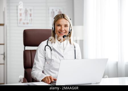 Telemedicine. Headshot portrait of smiling female doctor in headphones looking at camera. A female medical doctor remotely consults in a virtual Stock Photo