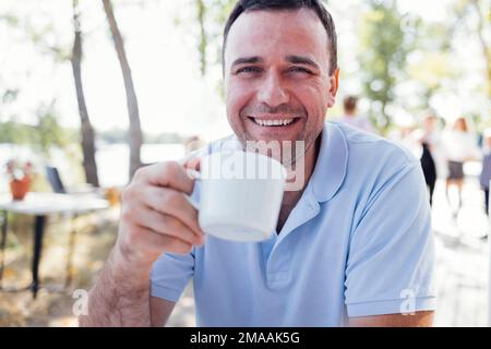 Happy man having a delicious coffee break at a outdoors cafe on the beach during a pleasant summer day Stock Photo