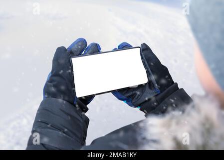 Phone in boy hands in horizontal position. Boy in a winter jacket, gloves and a cap. Isolated display for mockup. Winter time Stock Photo