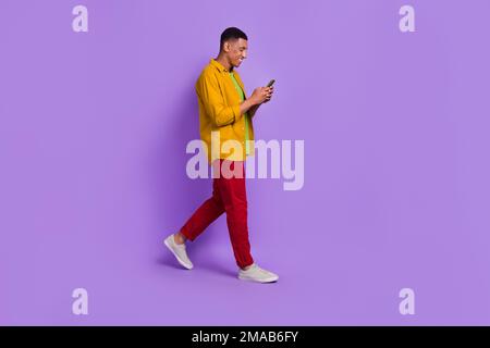 Full body profile portrait of cheerful man walking use telephone write typing isolated on purple color background Stock Photo