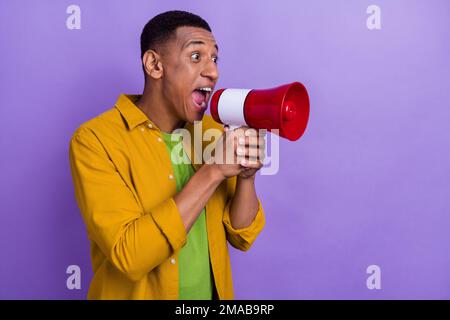Photo portrait of handsome young man hold megaphone scream excited dressed stylish yellow outfit isolated on violet color background Stock Photo