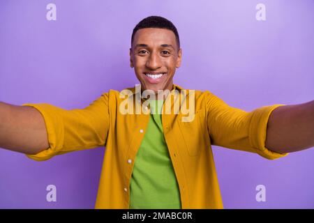 Photo portrait of handsome young man taking selfie toothy smile dressed stylish yellow clothes isolated on violet color background Stock Photo