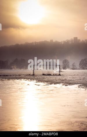 Soccer goal in a frozen puddle in the warm light of an early morning in winter in Germany, with fog in the background Stock Photo