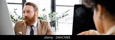 bearded businessman using computer near blurred african american colleague, banner,stock image Stock Photo