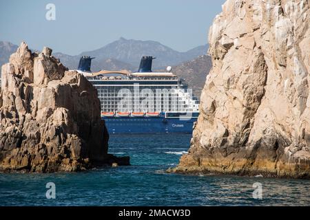 A cruise ship at anchor in the port of Cabo San Lucas, Mexican Riviera, is visible between the rocks and cliffs of Land's End at the tip of the Baja Stock Photo