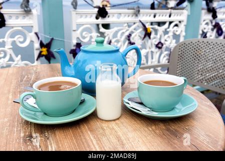 Two cups of tea with teapot and milk outside picnic table Stock Photo