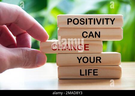 Positivity can change your life text on wooden blocks with hand and blurred nature background. Motivational concept Stock Photo