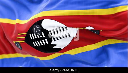 Eswatini national flag waving. The flag is blue, yellow, red stripes with black & white shield, staff and spears. Rippled fabric. Textured background. Stock Photo