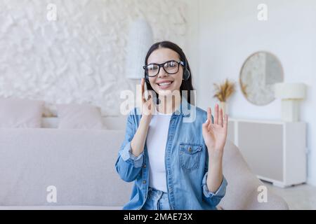 Online consultation. Young smiling woman working from home. Sitting on the sofa, talking into the camera through a headset, consulting, hotline, support and help line, online shopping. Stock Photo
