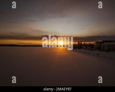 Sunset behind a snowy forest landscape and frozen river in Rovaniemi, Finland. Stock Photo