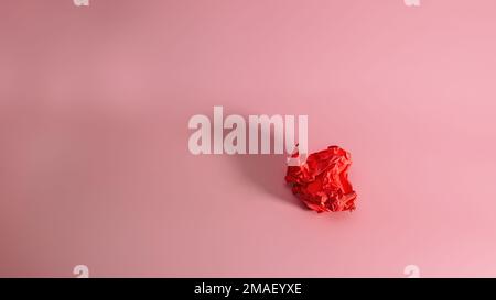 Crumpled red paper on a pink background with a trend shadow. Screwed up Craft Paper Ball. Junk paper can be recycle. Stock Photo