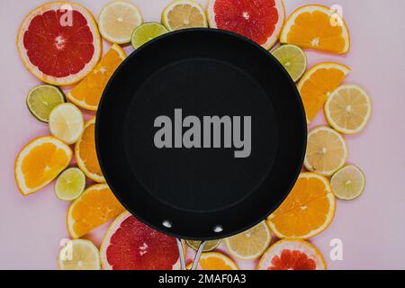 Black frying pan on sliced citrus plants. Oranges, grapefruit, lemon, lime on a pink background. flat lay Stock Photo