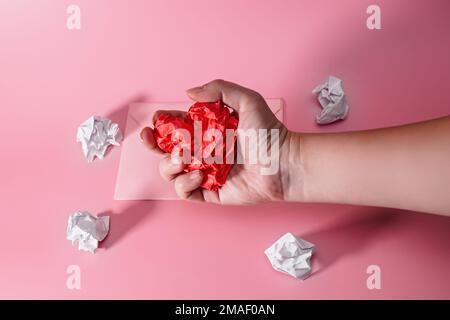 hand of aggressive and frustrated man squeezing heart out of crumpled paper. envelope with lumps of paper scattered. Letter to a Loved One on Valentin Stock Photo