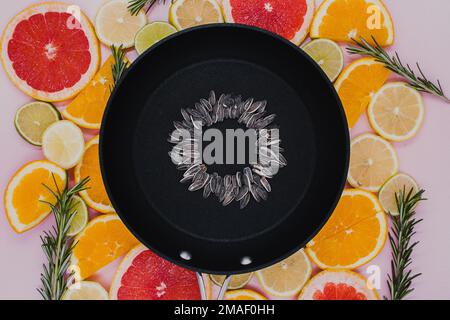 black frying pan with sunflower seeds, from which a sunflower flower is created on citrus plants cut into slices. Oranges, grapefruit, lemon, lime on Stock Photo