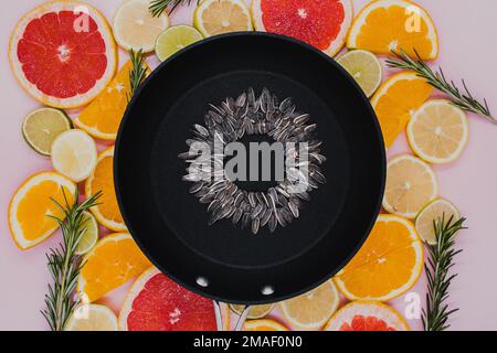 black frying pan with sunflower seeds, from which a sunflower flower is created on citrus plants cut into slices. Oranges, grapefruit, lemon, lime on Stock Photo