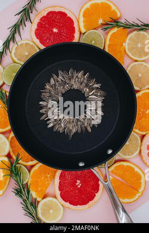 black frying pan with sunflower seeds, from which a sunflower flower is created on citrus plants cut into slices. Oranges, grapefruit, lemon, lime on Stock Photo