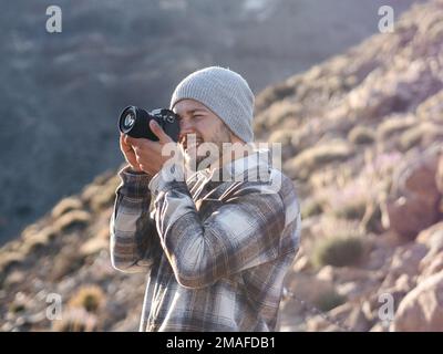 Young caucasian man taking photographs with camera in a flannel jacket and beanie. Stock Photo