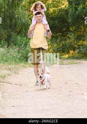 Father and daughter walking outside by countryside dirt road with pet dog on waist leash Stock Photo