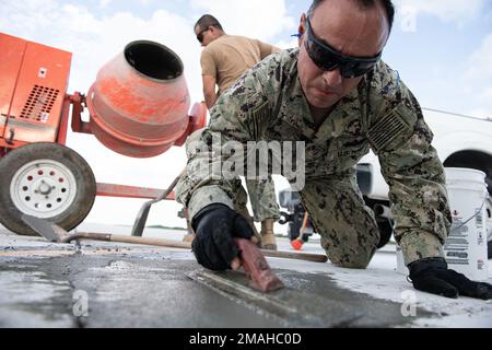 (220526-N-OI810-0233) KEY WEST, Florida (May 26, 2022) Steelworker 1st Class Leonardo Gomez, from Bogota, Colombia, assigned to Naval Mobile Construction Battalion (NMCB) 14, uses a finishing trowel to smooth concrete as Seabees repair a damaged section of runway at Boca Chica Field, Naval Air Station Key West (NASKW), May 26, 2022. NMCB-14 teamed up with NASKW Public Works and NASKW Air Operations Department to complete the needed airfield damage repair. Seabees assigned to NMCB-14 travelled to NASKW to perform on-site training and assist with facility and compound maintenance. NMCB-14 provid Stock Photo