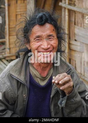 Ziro, Arunachal Pradesh, India - 02 24 2009 : Portrait of friendly smiling Apatani tribal man with traditional frontal hair bun and chin tattoo Stock Photo