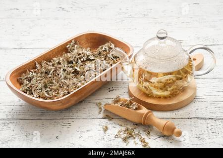 Glass teapot of herbal Icelandic moss tea. Wooden scoop and bowl of dried Iceland moss on white table. Cetraria islandica - latin name of plant. Alter Stock Photo