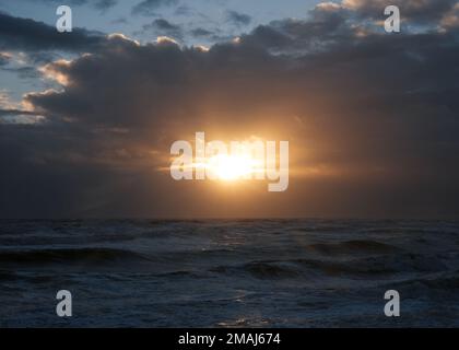 Sunburst through clouds while setting over the English Channel. - St Leonards On Sea, UK Stock Photo