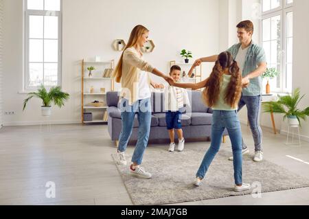 Happy family with two children are playing leading a round dance at home in living room. Stock Photo
