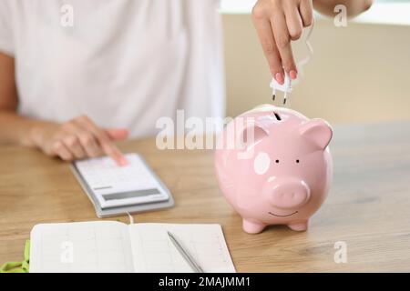 Woman connects electric plug to piggy bank and counting money on calculator. Stock Photo