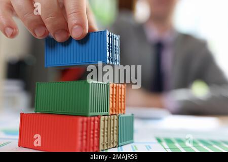 Business man arranging stack of freight cargo containers on office desk with financial documents. Stock Photo