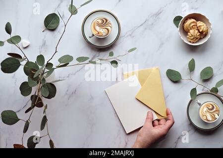 Greeting card mockup background. Mint green postal envelope, blank white card, pen and office stationary. Eucalyptus twigs on stone, overhead view Stock Photo