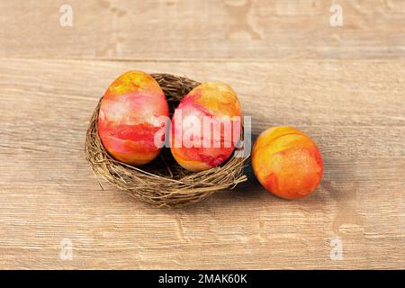 Three Easter eggs in a decorative nest of sisal on a wooden background. Happy Easter concept. Greeting card. Stock Photo