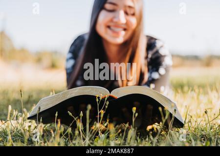 Close up of a young woman lying while reading the bible on the grass with a blurred background  Stock Photo