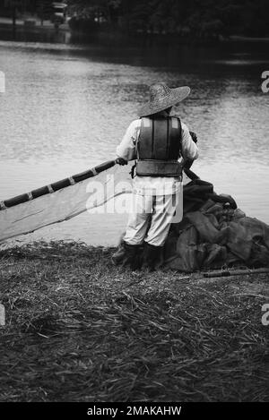 A vertical shot of an old man in rustic clothes working by the lake Stock Photo