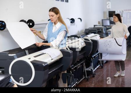 Woman using printer while working in print shop Stock Photo