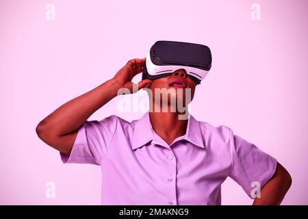 Happy young black lady in VR glasses exploring cyberspace, touching imaginary screen, playing virtual reality game in neon light. Positive African Ame Stock Photo