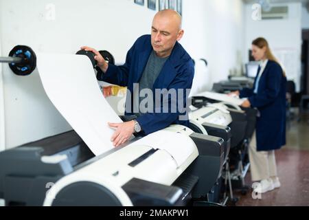 Service man uses plotter and checks functionality in printing shop Stock Photo