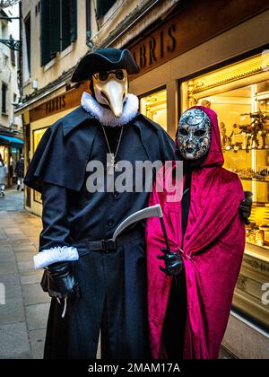 A man in a plague doctor costume and a woman in a death costume stand on an evening street in Venice, Italy Stock Photo