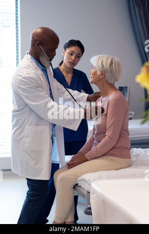 Vertical of diverse senior male doctor using stethoscope examining senior female patient, copy space Stock Photo
