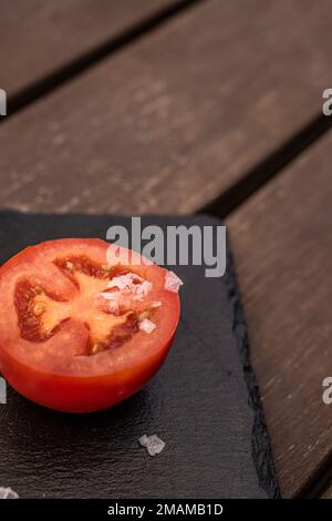 A ripe tomato split in half with sprinkles of coarse salt on a black slate Stock Photo