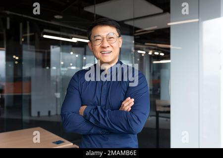 Portrait of successful asian boss inside office, businessman with crossed arms smiling and looking at camera, man in shirt and glasses happy with result of achievement at work. Stock Photo