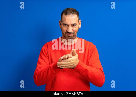 Latino handsome man feeling proud, mischievous and arrogant while hatching an evil plan or thinking up a trick. Isolated on blue background. Stock Photo