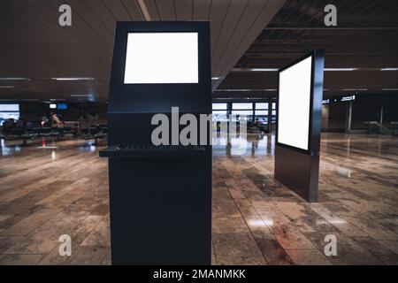 A wide-angle view of an internet station terminal mockup in a waiting room with shiny brownstone flooring on an airport with a blank billboard templat Stock Photo