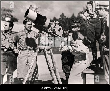 Leni Riefenstahl Film Director looking through the lens of a movie camera for the Nazi propaganda film Triumph of the Will in 1934 on location at Reichsparteitagsgelände (Nazi party rally grounds) in Nuremberg, Franconia, Germany. On the left of the camera her chief cameraman Sepp Allgeier (1895–1968) kept an eye on her. – Members of Riefenstahl's team wore a SA uniform or similar looking clothes (Allgeier) in order to keep the overall view of the rally as the deployed groups were all uniformed. Stock Photo